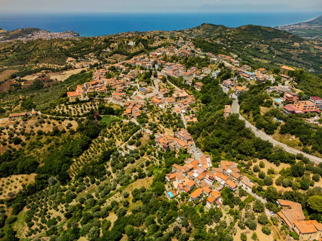Vista aerea del borgo di Ogliastro Cilento tra gli ulivi, con il mare all'orizzonte